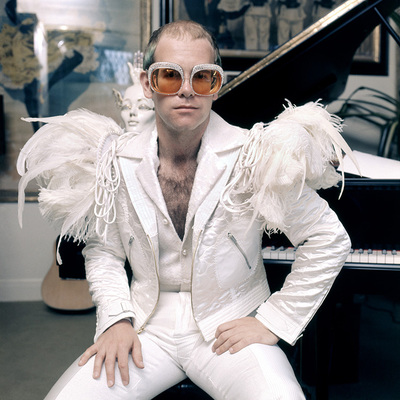 English pop singer Elton John in a flamboyant stage outfit of white suit with feather trim and rhinestone encrusted glasses, circa 1973.
