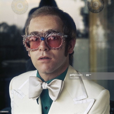 English pop singer Elton John in a white jacket and rococco spectacles, circa 1978.
