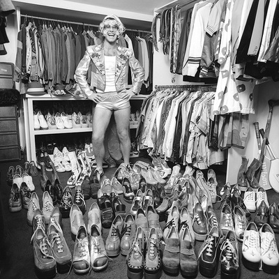 Elton John at home in London, 1975, with part of his wardrobe, notably a large collection of platform shoes.
“That’s a great one. When I was at his home, I suggested we just walk around and I’ll take some photos of him with some of his collections. I was thinking at the time, he’ll show me some sculptures or paintings. Little did I know what I was getting myself into!” – Terry O’Neill
