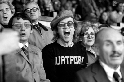 Watford FC manager Graham Taylor and pop singer Elton John cheer and spectate during a football match, late 1980s.
